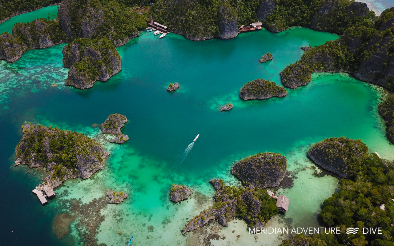 Aerial view of a turquoise lagoon in Raja Ampat surrounded by small limestone islands with a boat moving through the water.